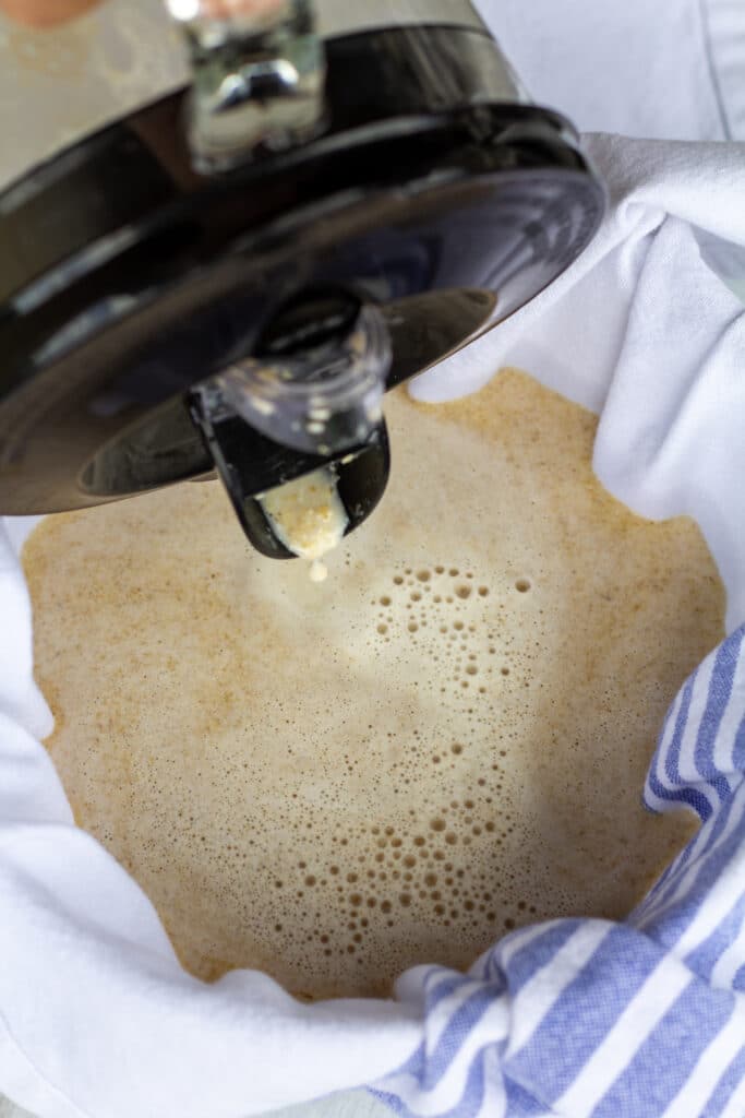 oat milk being poured in a strainer in a bowl