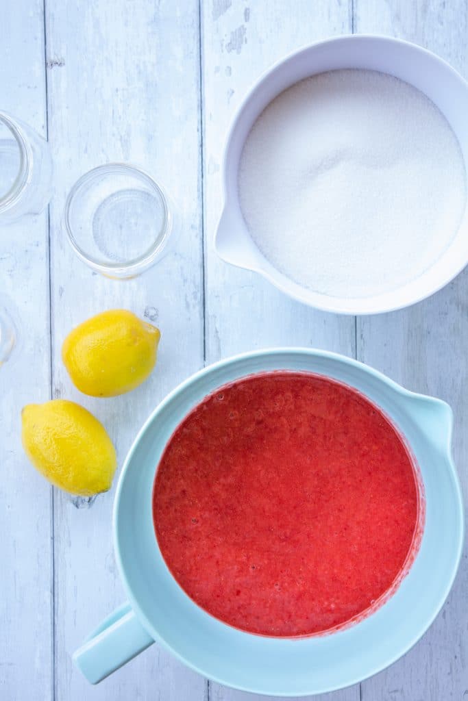 strawberries, sugar, lemons, and jars on a white background