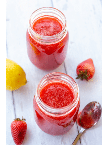 strawberry jam in jars on a white background with lemons and strawberries on the side