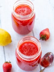 strawberry jam in jars on a white background with lemons and strawberries on the side