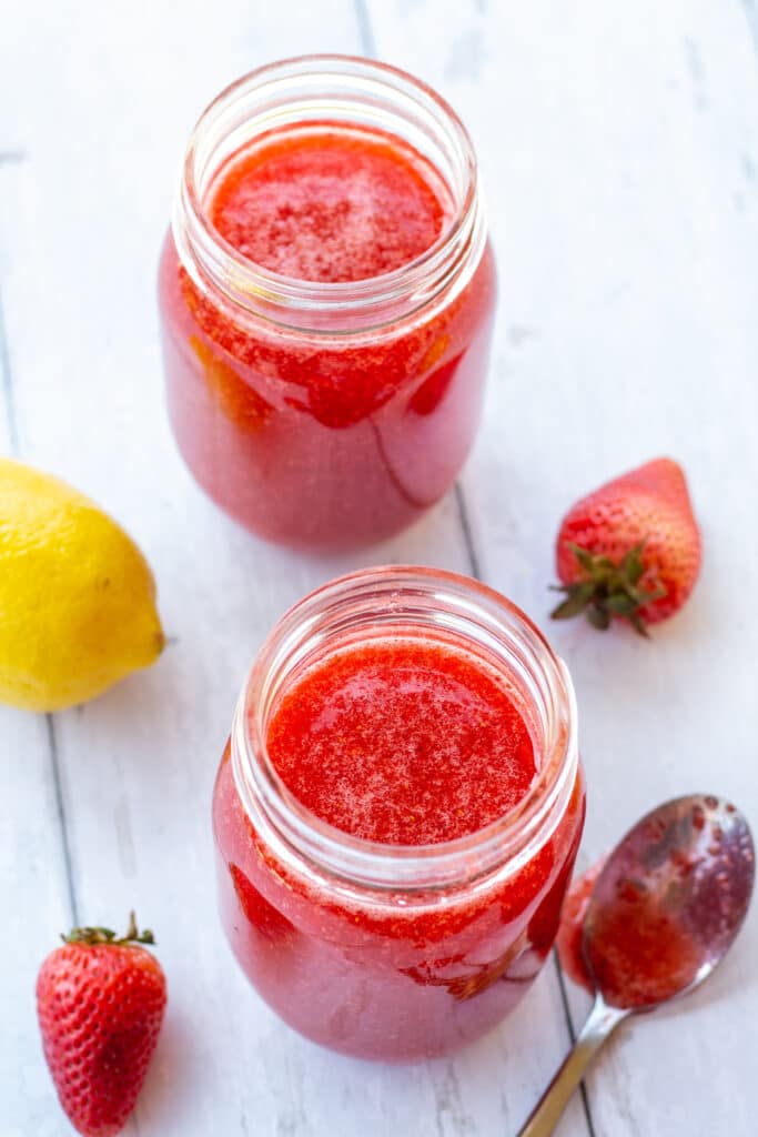 strawberry jam in jars on a white background with lemons and strawberries on the side