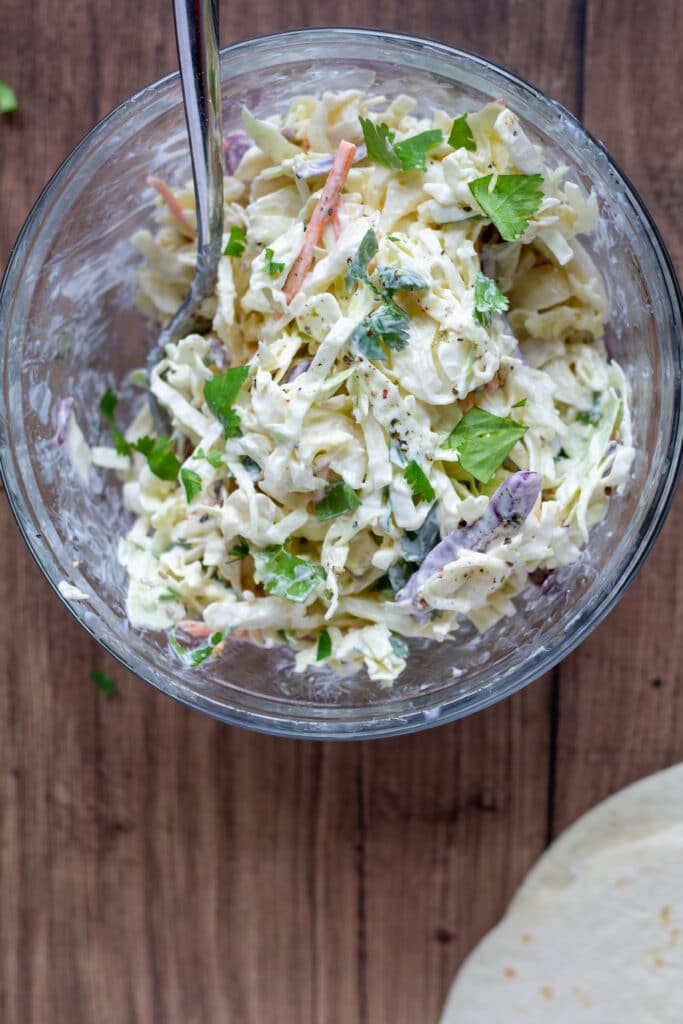 coleslaw in a clear glass bowl on a wood background