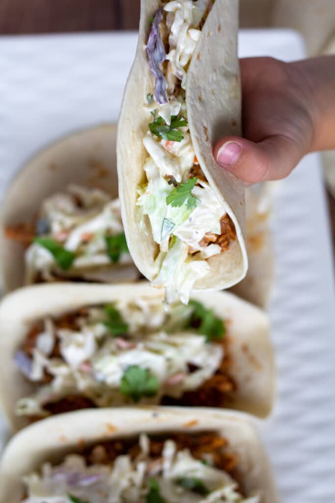 taco held by a hand over a white plate of tacos