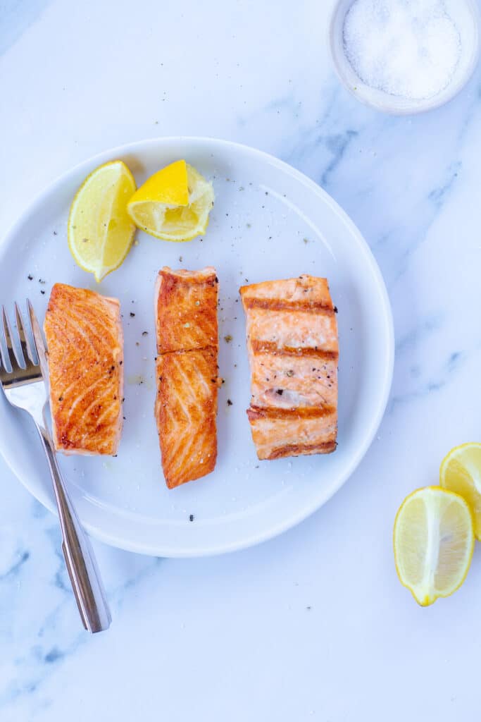 Three pieces of salmon on a white plate next to lemons 