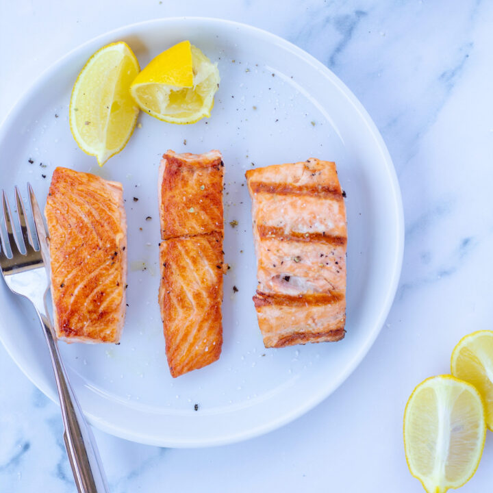 Three pieces of salmon on a white plate next to lemons