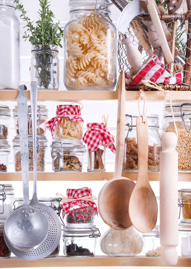 an organized pantry with jars of pasta, hanging spoons, and a jar of green leaves