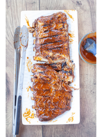 grilled BBQ pork ribs on a white plate brushed with sauce