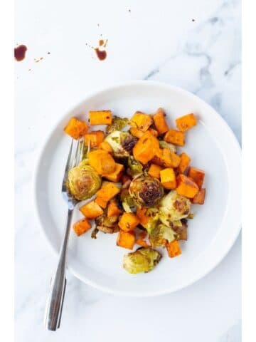 A white plate topped with root veggies with a silver spoon resting on the plate