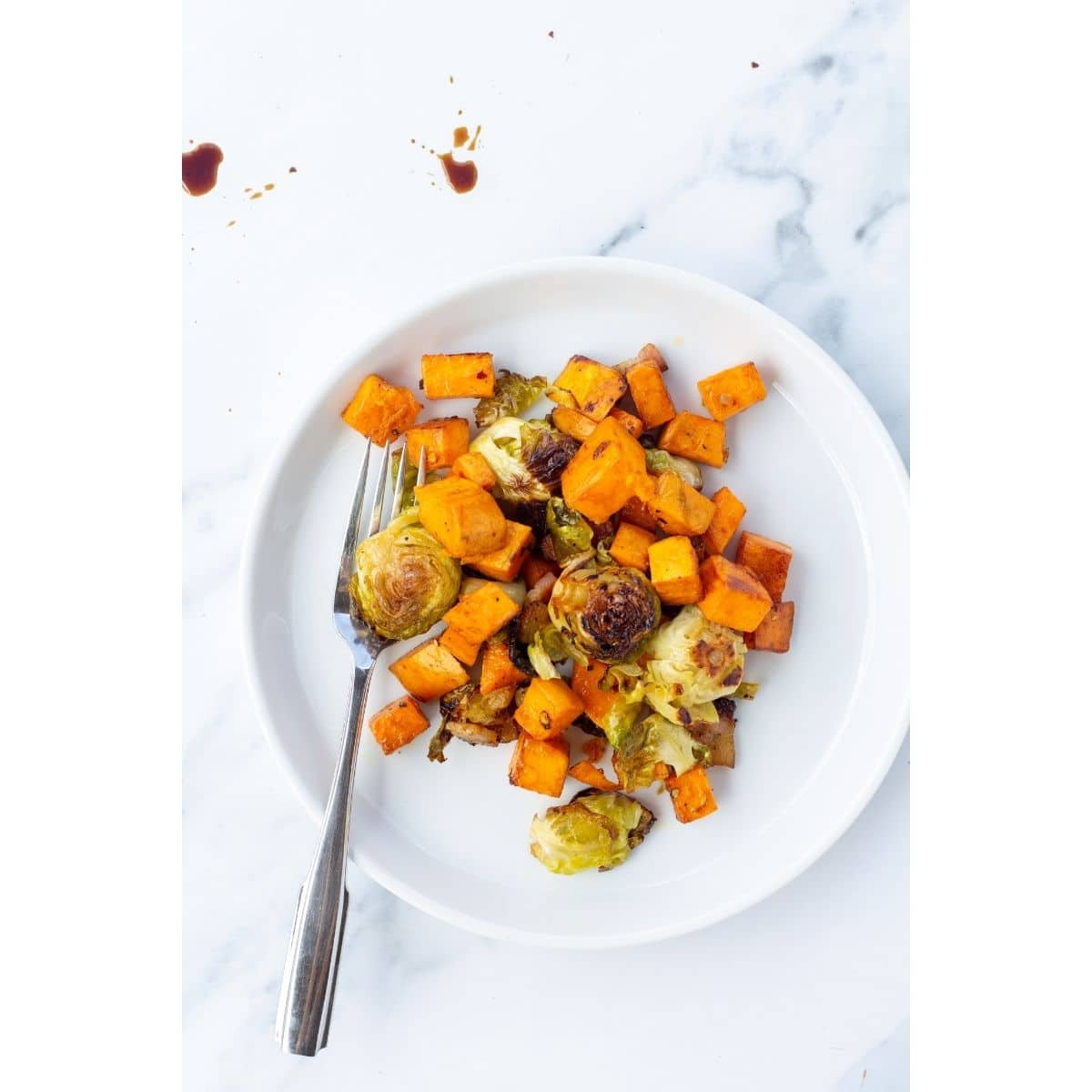 A white plate topped with root veggies with a silver spoon resting on the plate