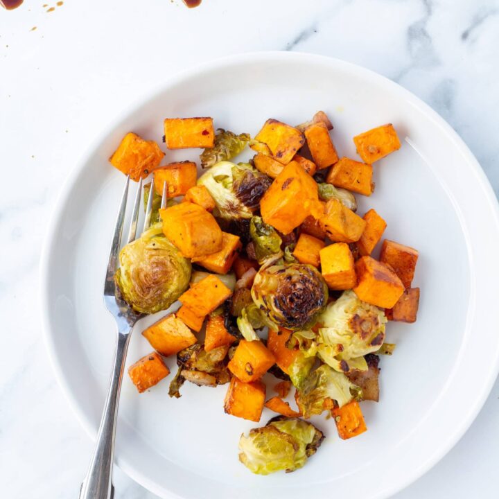 A white plate topped with root veggies with a silver spoon resting on the plate