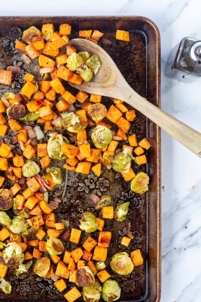 Ingredients on a sheet pan with a wooden spoon before roasting