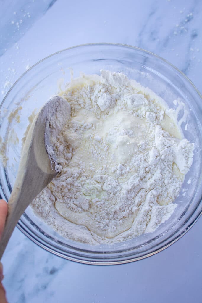 mixing flour and cream together in a glass bowl on a white marble counter