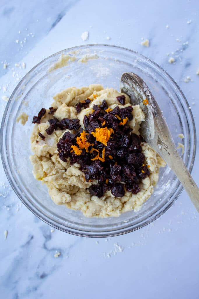 Cherries, orange zest, and orange juice added into the flour mixture in a glass bowl