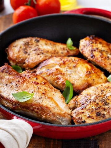 red pan with cooked chicken breasts with basil leaves on top