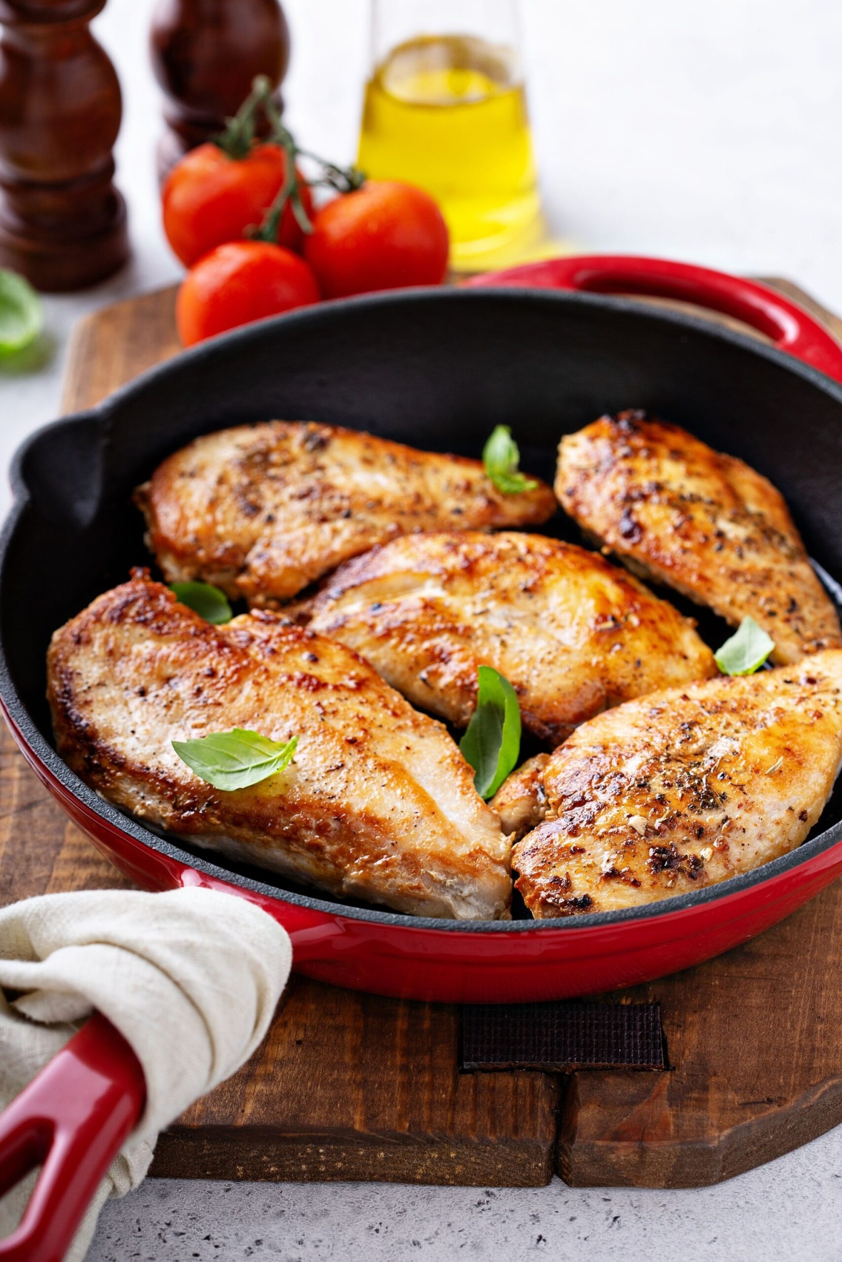 red pan with cooked chicken breasts with basil leaves on top