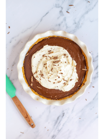 chocolate pie topped with whipped cream and chocolate shavings sitting on a white marble counter