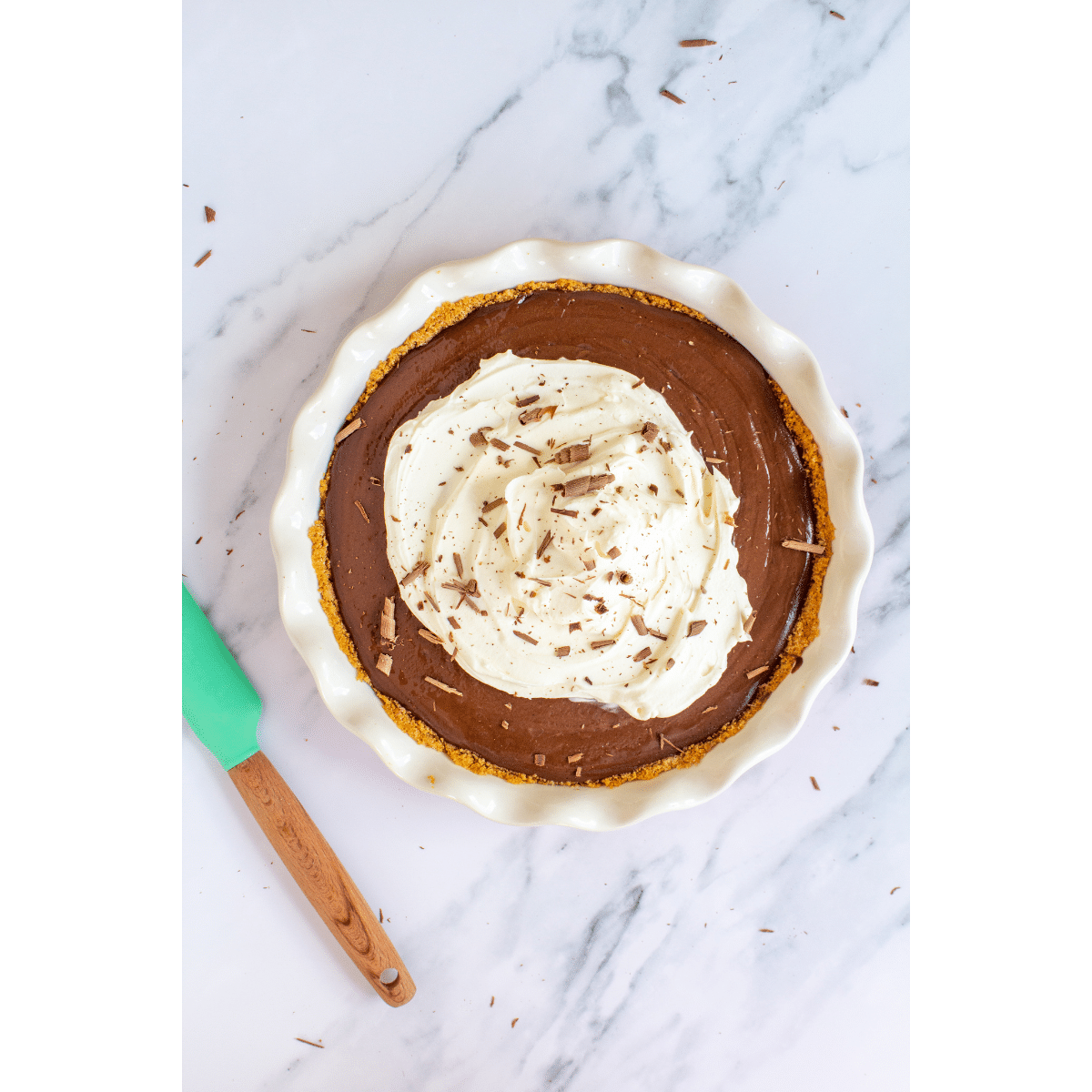 chocolate pie topped with whipped cream and chocolate shavings sitting on a white marble counter