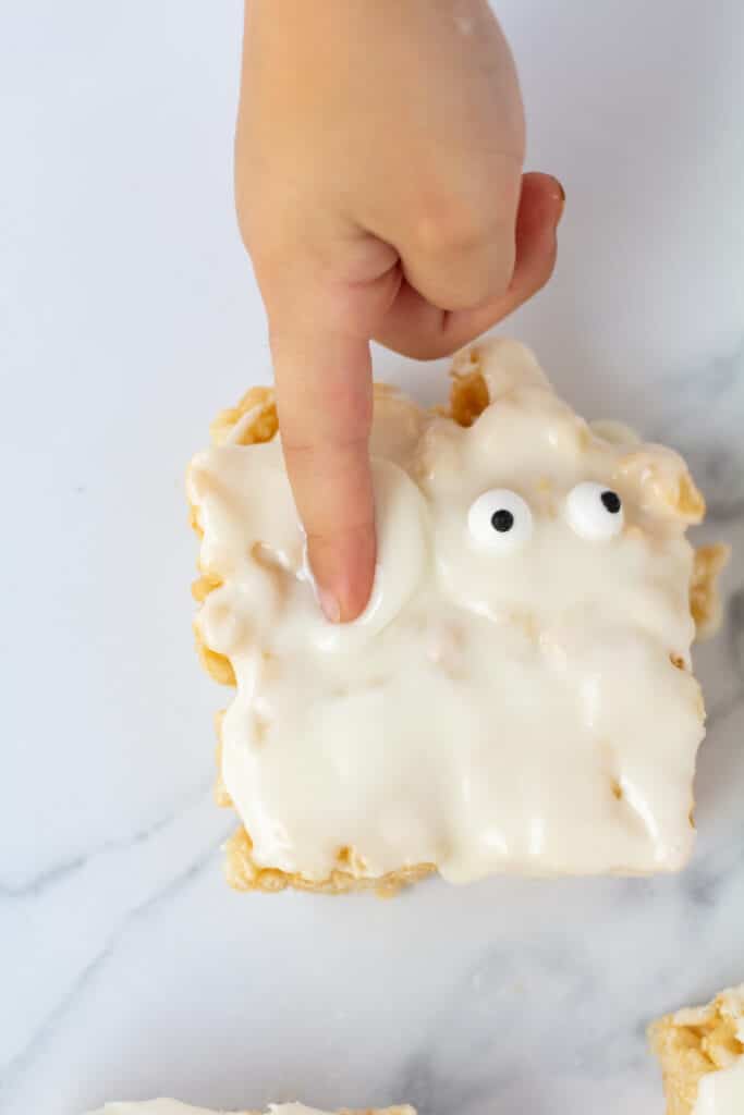 A child's finger in the icing of a mummy rice crispy treat