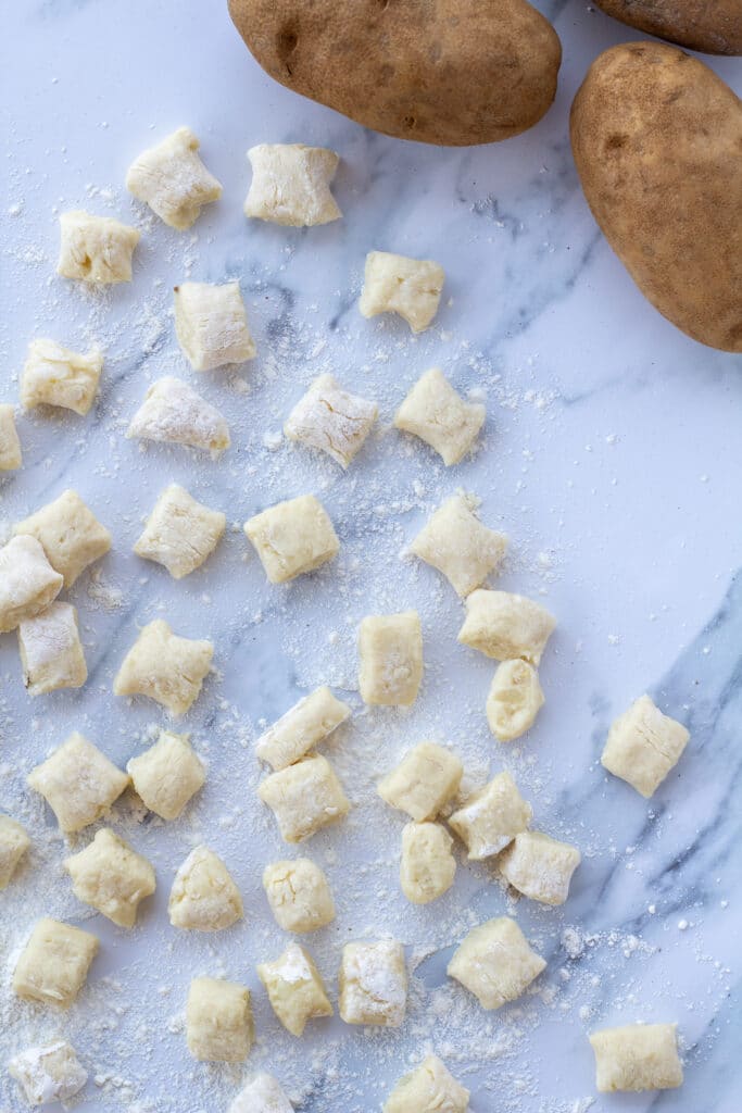 gnocchi pillows on a white counter next to potatoes