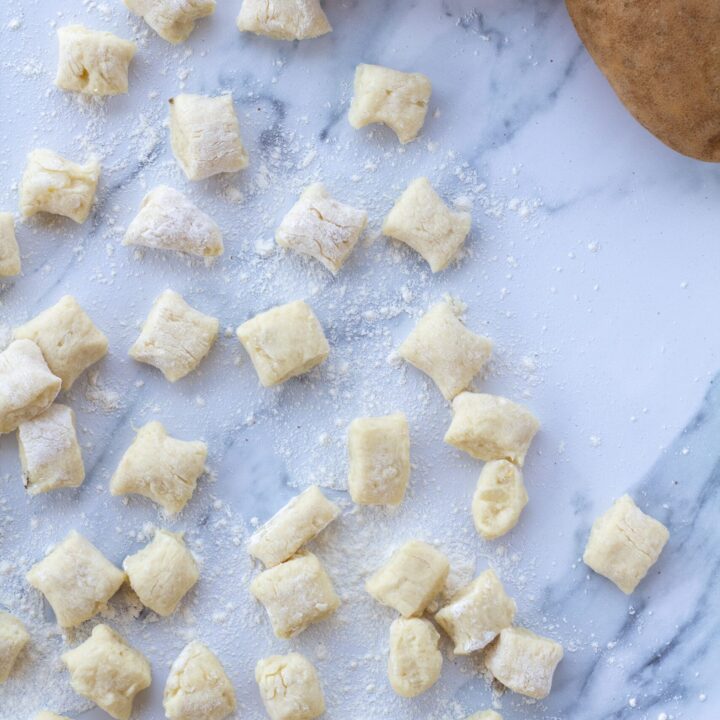 gnocchi pillows on a white counter next to potatoes