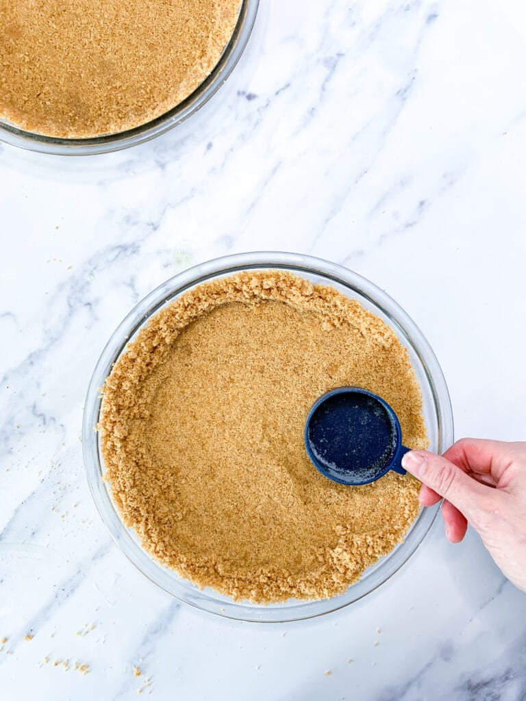 pie crust being packed down with a blue measuring cup on a white marble counter