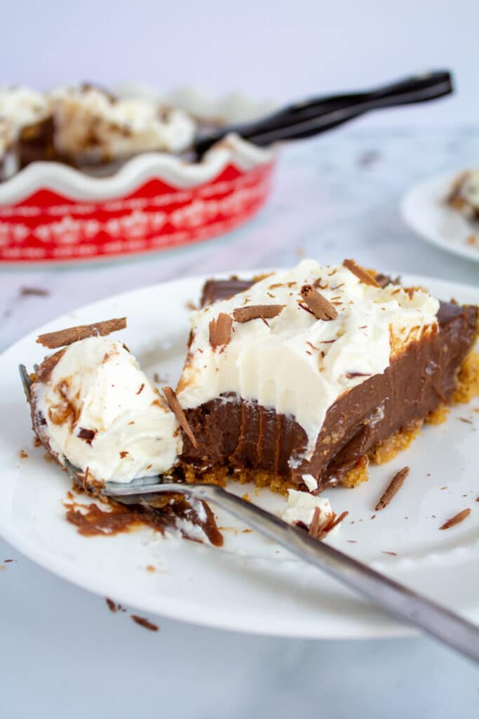 a slice of chocolate pie with whipped cream on a white plate with a fork