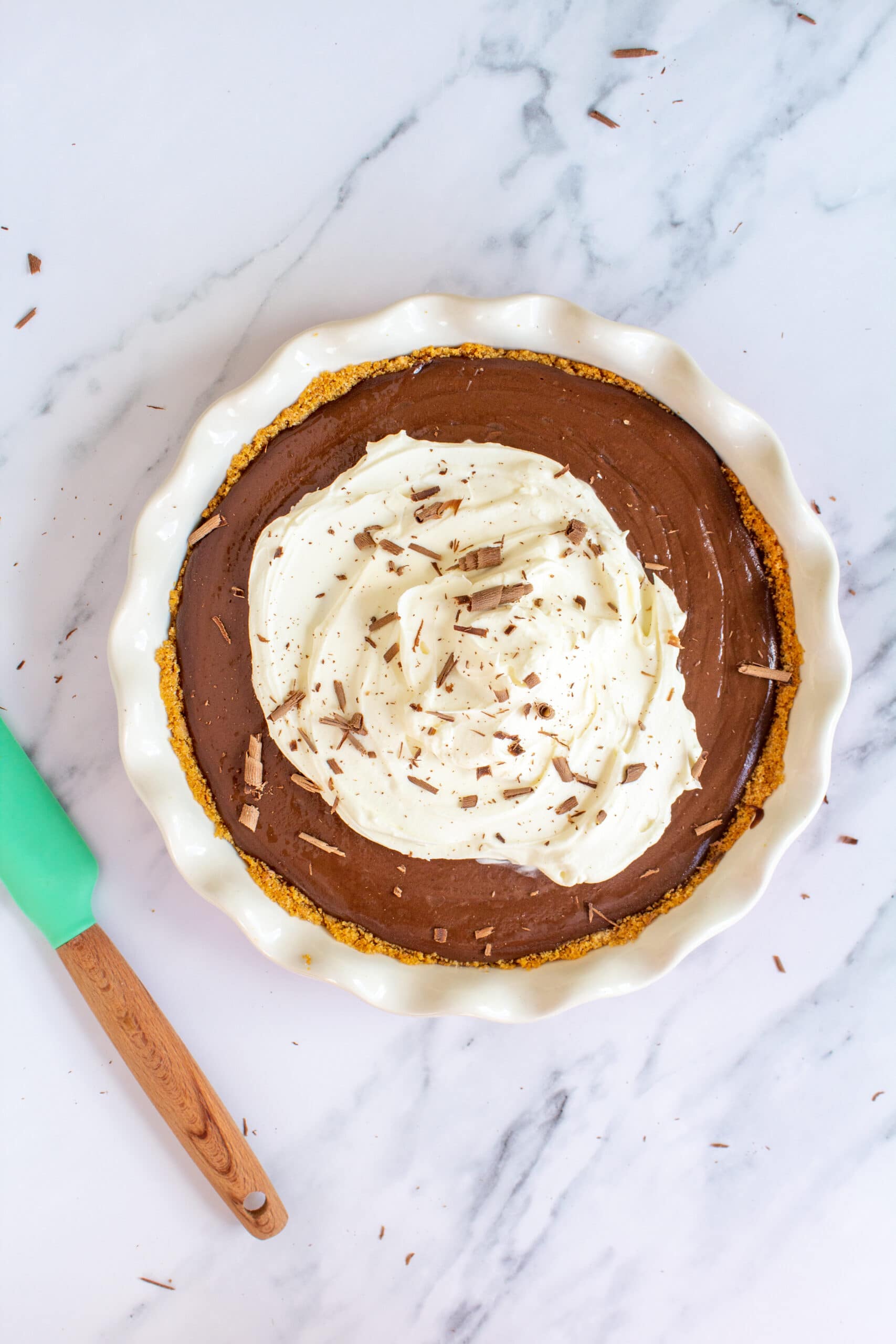 chocolate pie topped with whipped cream and chocolate shavings sitting on a white marble counter