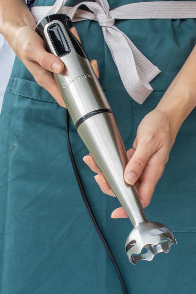 a woman wearing an apron holding an immersion blender