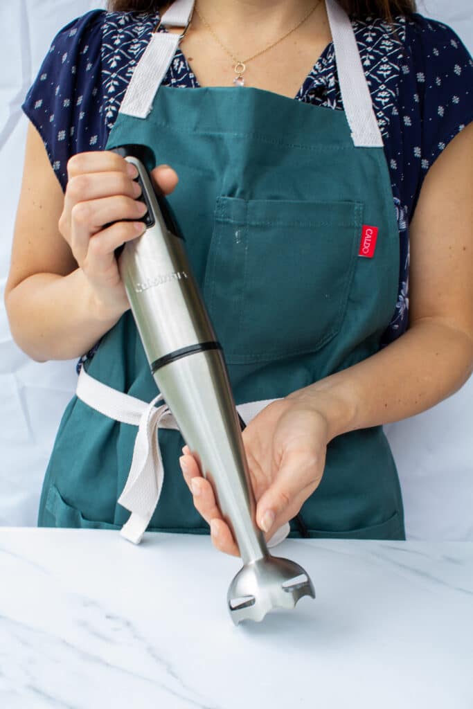 a woman holding an immersion blender with two hands