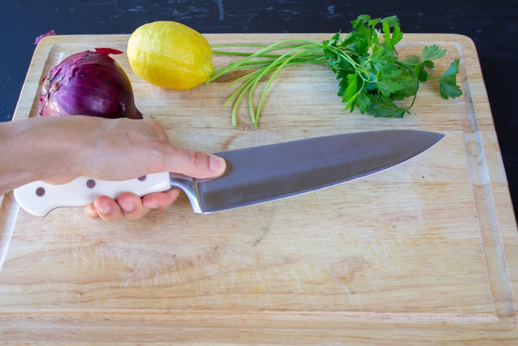 hand holding a chef's knife with thumb on blade