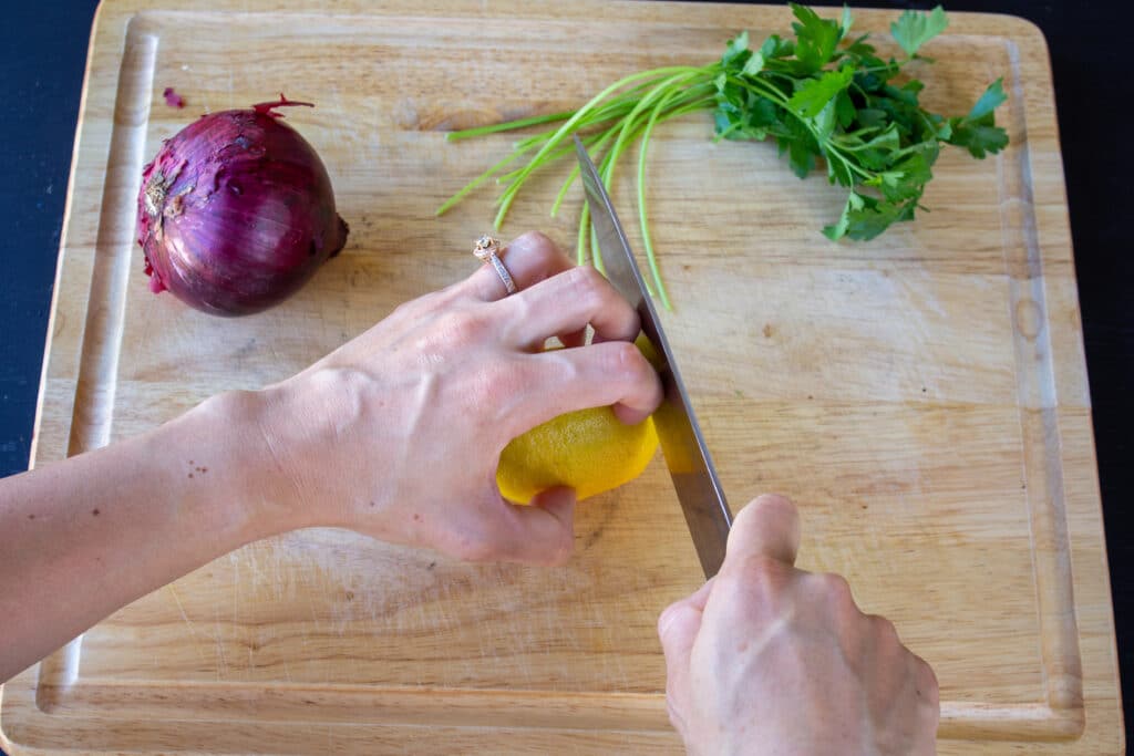 two hands cutting a lemon with a knife on a cutting board