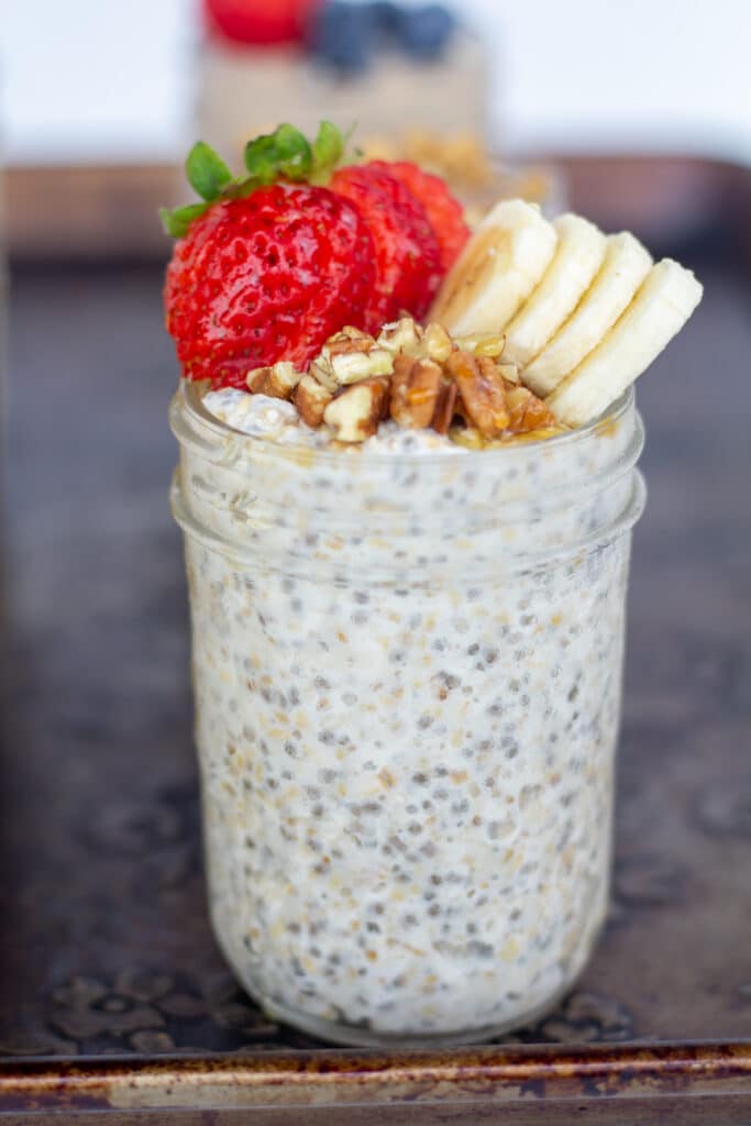 straight on view of oats in a jar topped with strawberries, bananas, and pecans