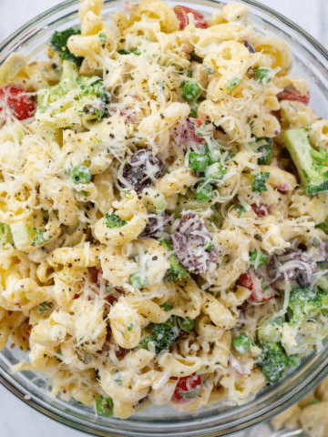 a bowl of healthy creamy bow tie pasta salad overhead next to a large spoon and two cherry tomatoes