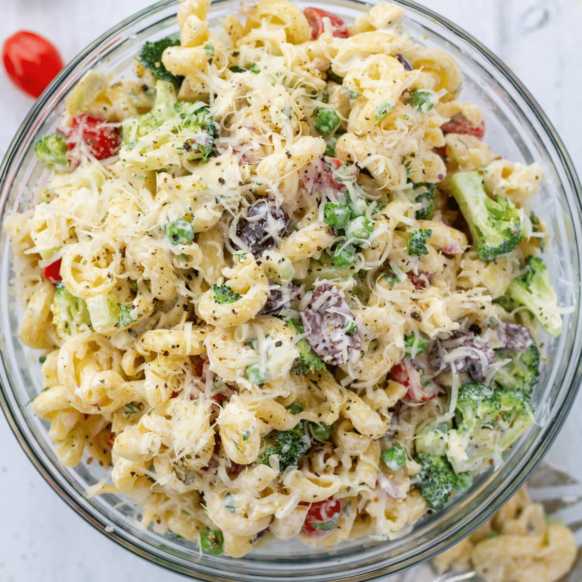 a bowl of healthy creamy bow tie pasta salad overhead next to a large spoon and two cherry tomatoes