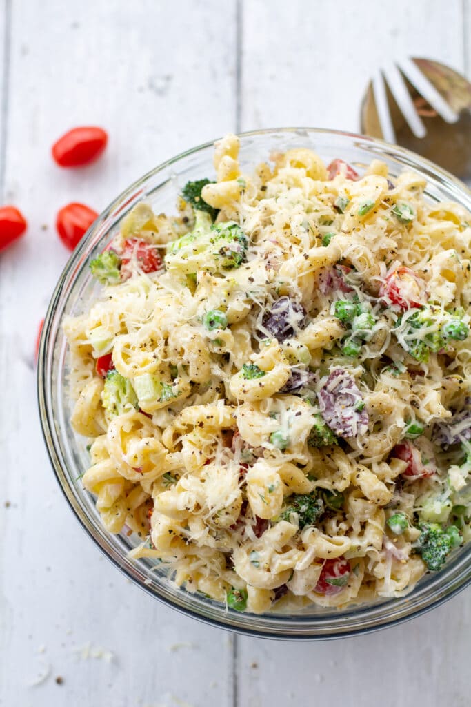 a glass bowl of healthy creamy bow tie pasta salad topped with shredded parmesan cheese