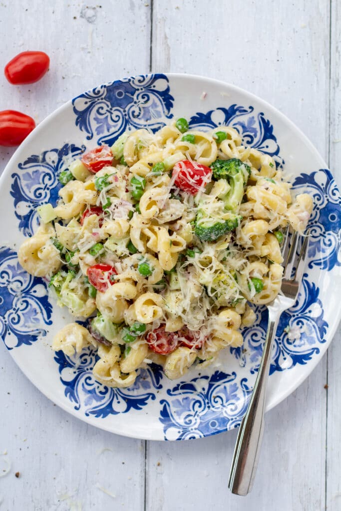 pasta salad on a blue and white plate with a fork on a white surface