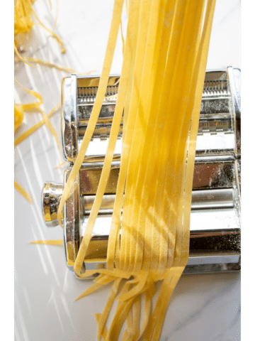 strands of pasta held over a pasta machine