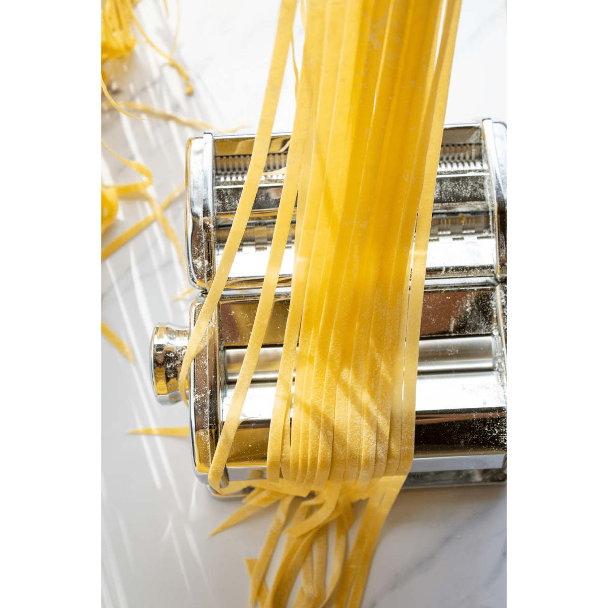 strands of pasta held over a pasta machine