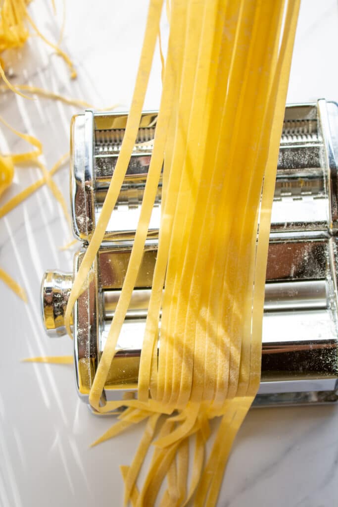 strands of pasta held over a pasta machine