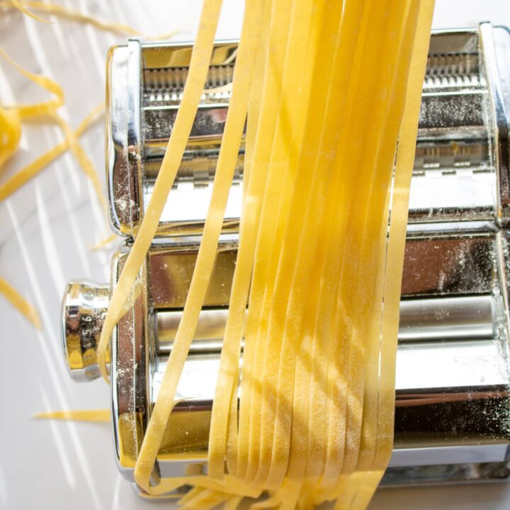 strands of pasta held over a pasta machine