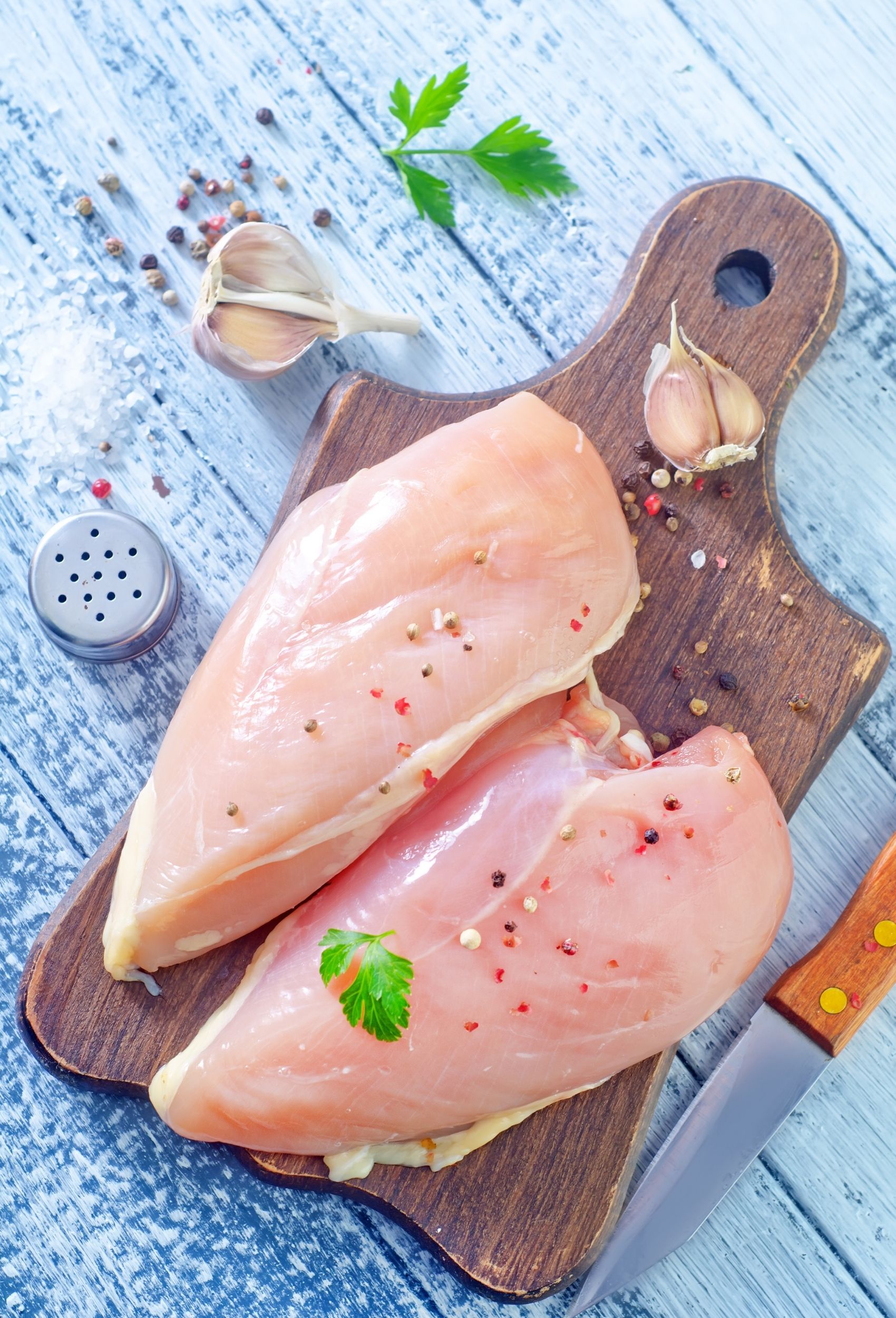 raw chicken breasts with spices sprinkled on top on a cutting board