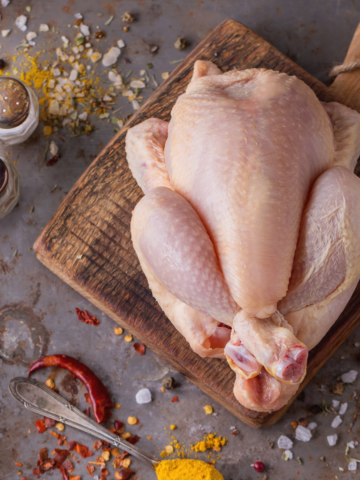 whole chicken on a cutting board surrounded by spices