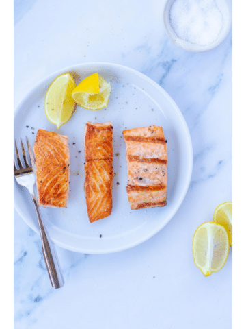 Three pieces of salmon on a white plate next to lemons