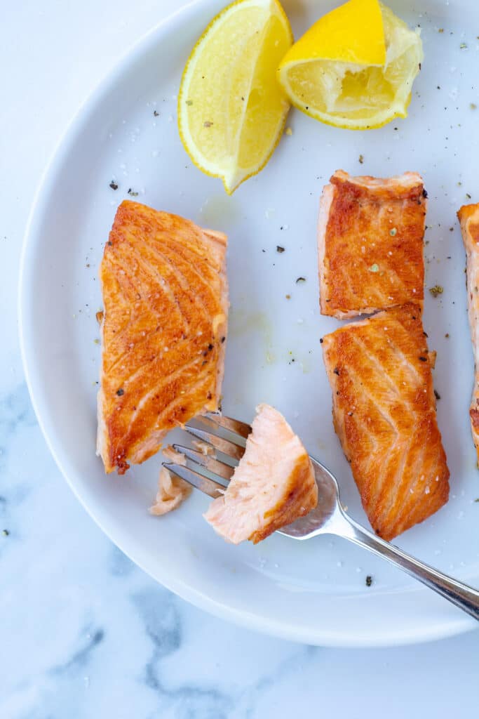 Three pieces of salmon on a white plate with a bite taken out of one