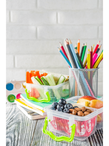 a lunch box with food on a wood surface with a cup of colored pencils sitting next to it