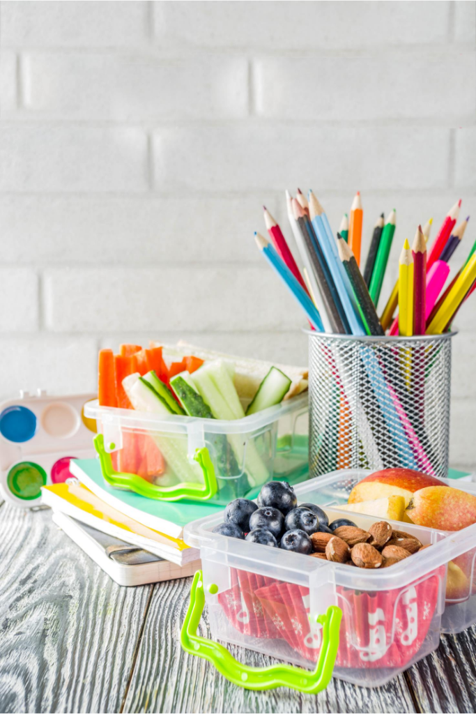 a lunch box with food on a wood surface with a cup of colored pencils sitting next to it