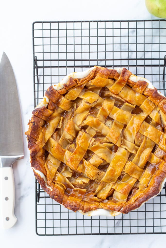 A whole apple pie sitting on a cooling rack next to a knife