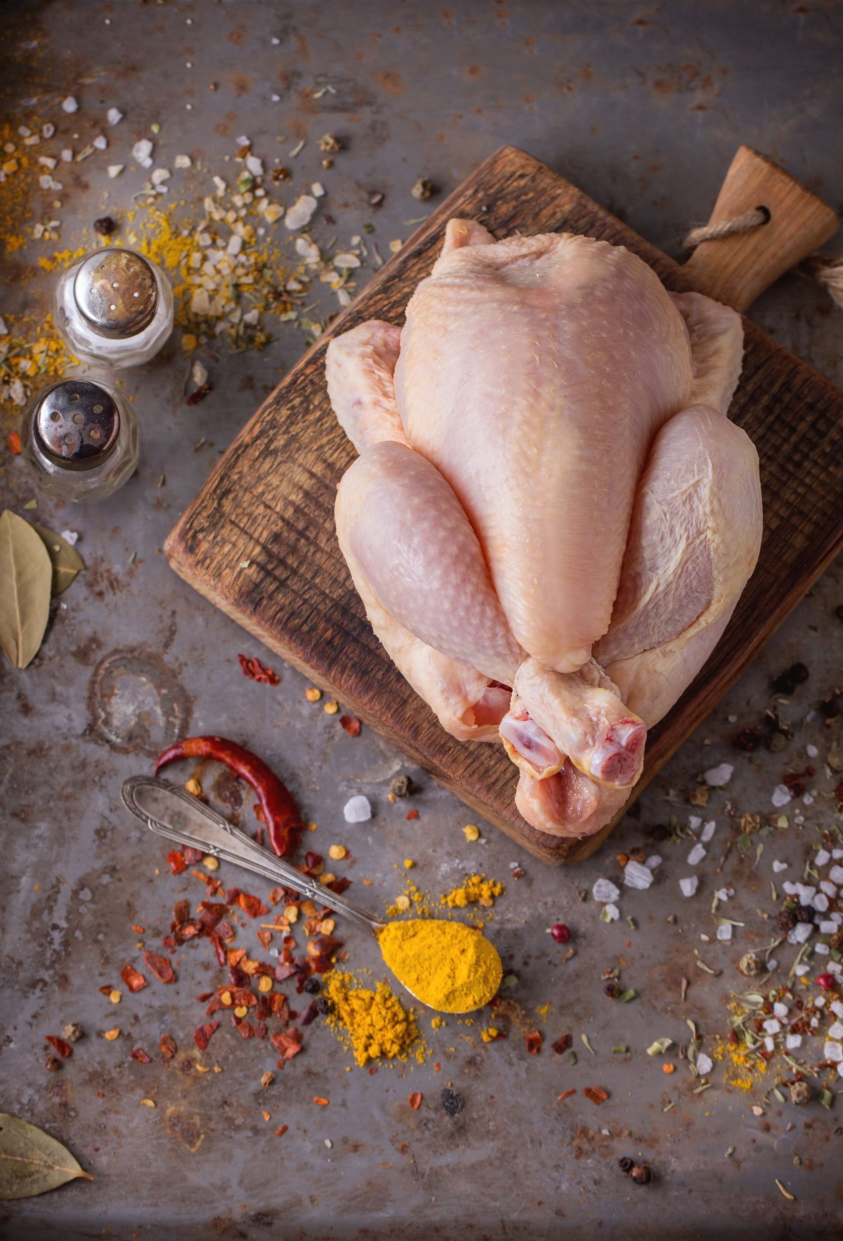 whole chicken on a cutting board surrounded by spices
