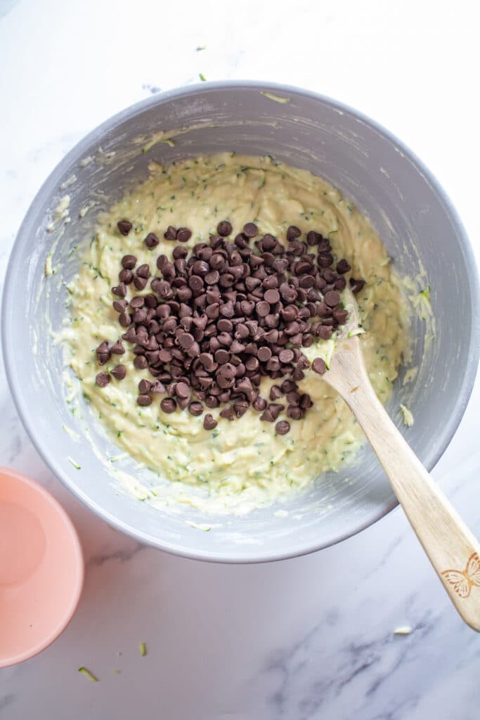 A bowl of batter with chocolate chips and a wooden spoon