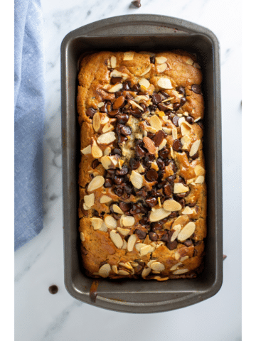 Zucchini bread in a loaf pan next to a blue cloth napkin on a marble surface